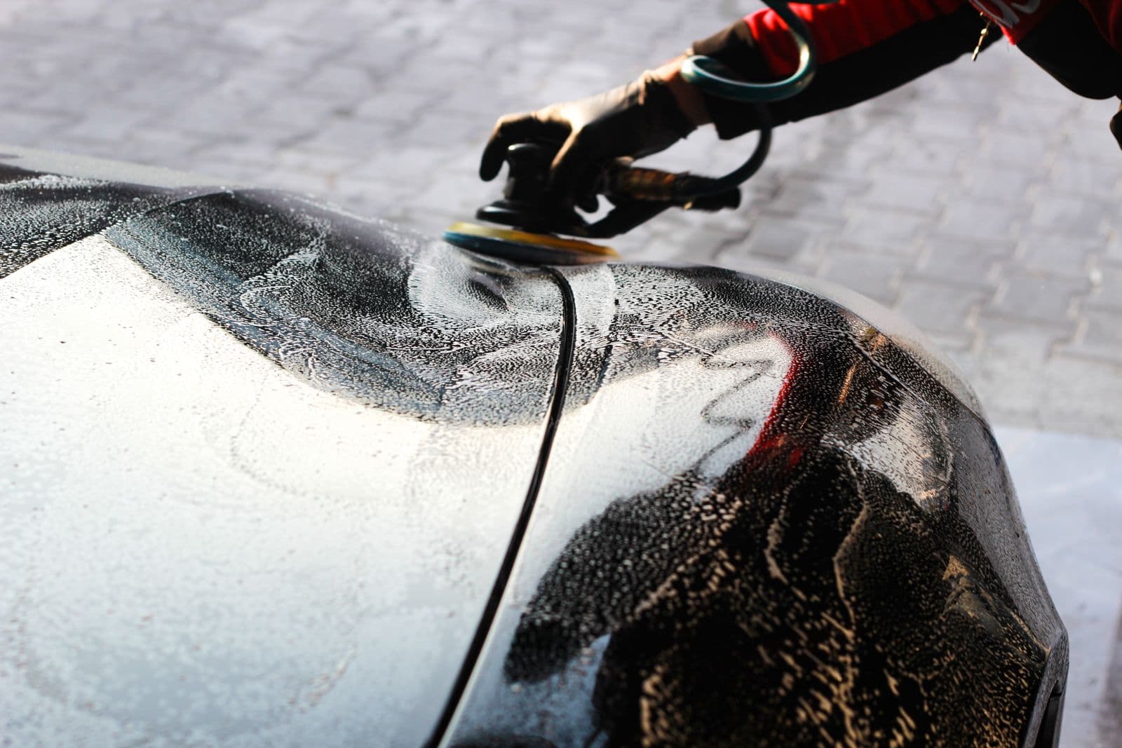 Detailer using a machine polisher on a soapy car body panel