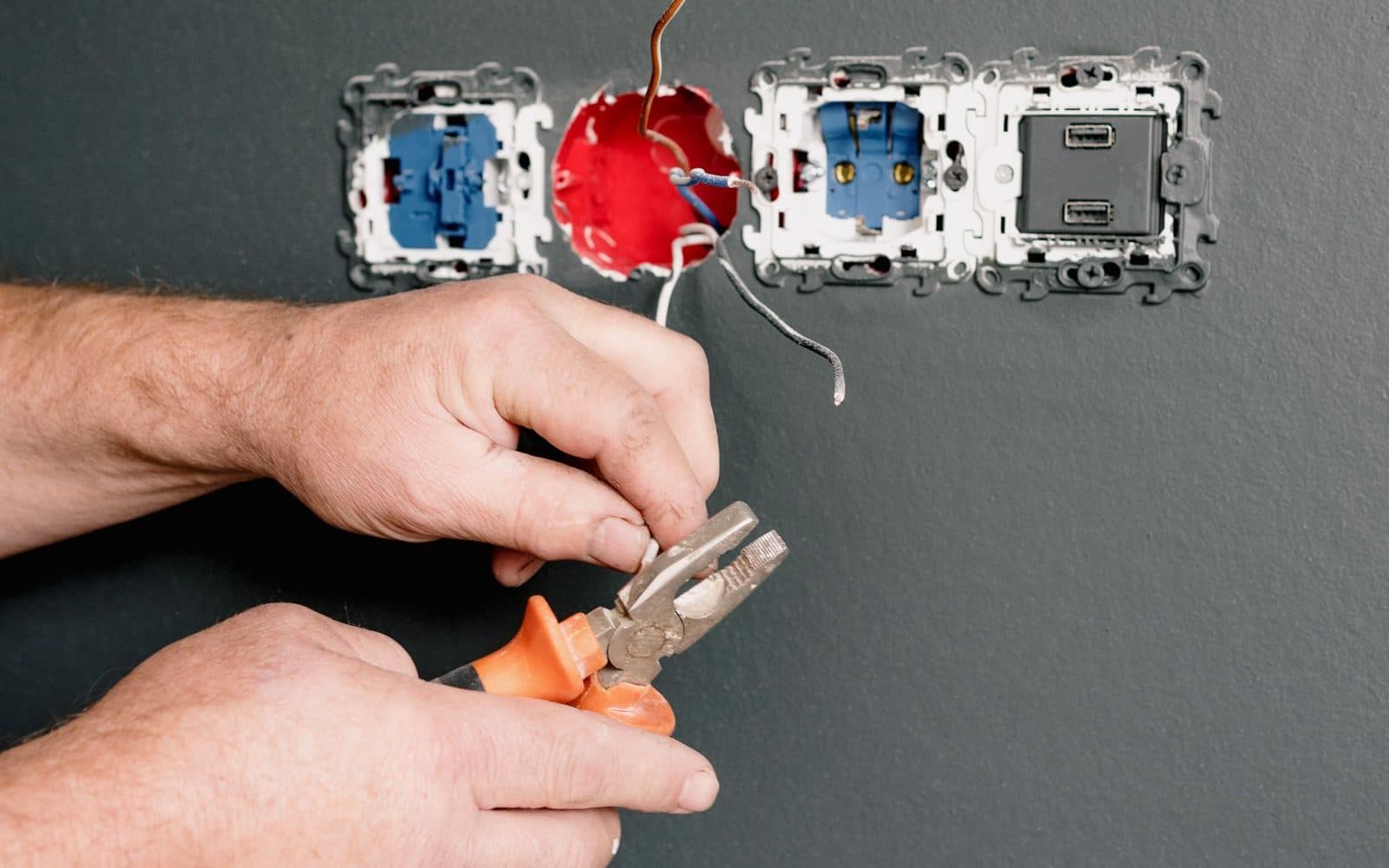 Electrician stripping wires with pliers beside open wall sockets